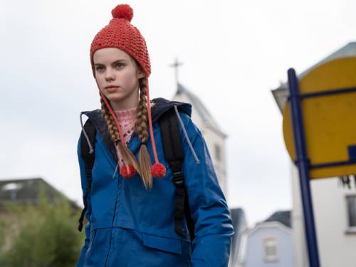 ein 12jähriges Mädchen mit roter Pudelmütze und blauem Anorak geht eine Straße entlang.